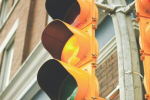A traffic light on yellow, with a brick building behind it.